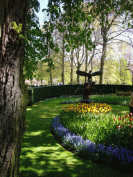 Blue, yellow and red flowers and a statue in a grassland near the central lake of the Keukenhof park