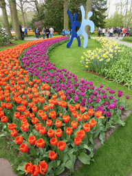 Red and purple tulips, other flowers and a piece of art in a grassland near the central lake at the Keukenhof park