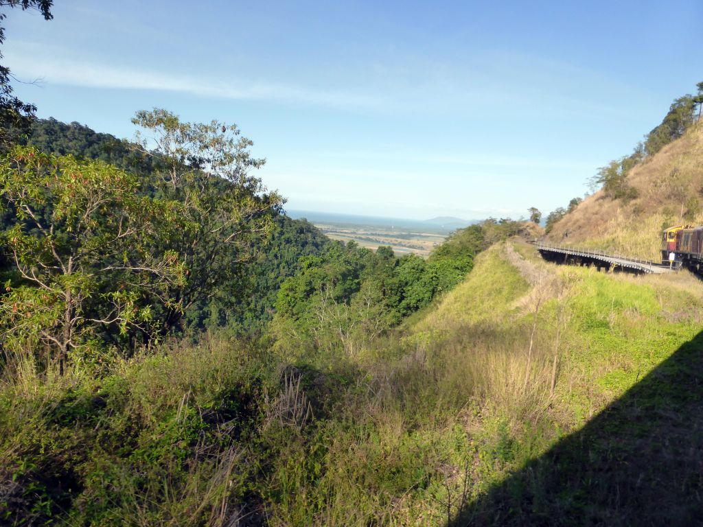 Hills with trees on the other side of the Barron Creek valley, and the Kuranda Scenic Railway train near the Red Bluff rocks