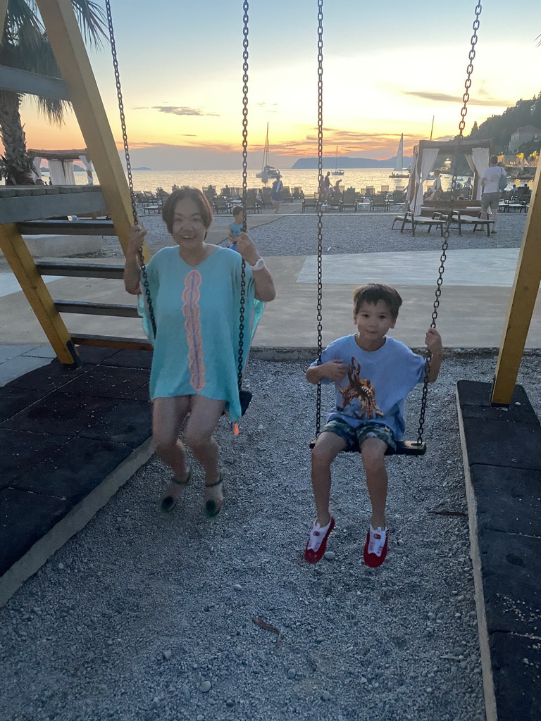 Miaomiao and Max on swings at the Uvala Lapad Beach, at sunset