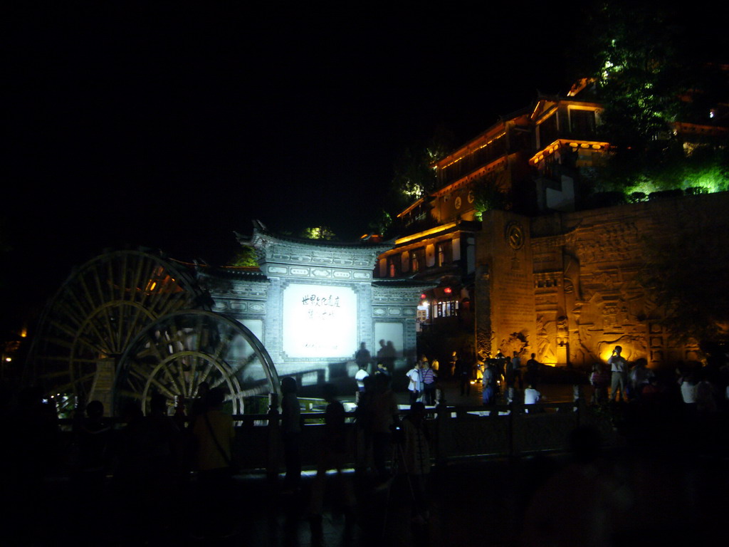 Water wheel, wall with inscriptions, stone wall and Qian Xue Lou Hotel at Yuhe Square in the Old City of Lijiang, by night