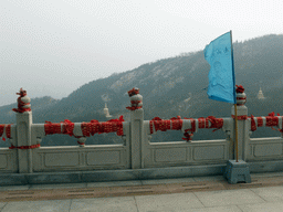 Flag and decorations at the east side of the highest platform at the Nanshan Great Buddha, with a view on the surroundings hills and towers