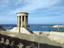 The Siege Bell Monument with the World War II Memorial, the Grand Harbour and Fort Ricasoli, viewed from the Lower Barracca Gardens at Valletta