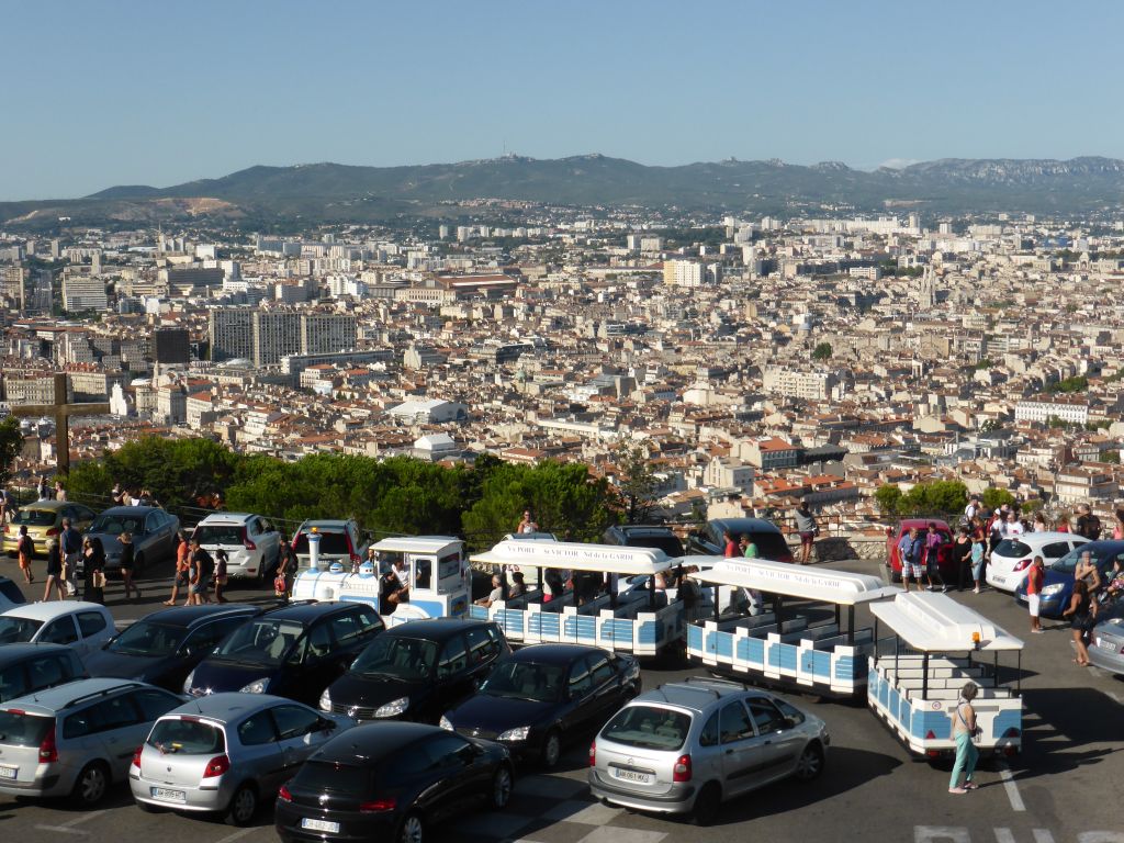 Tourist train and wooden cross at the square in front of the Notre-Dame de la Garde basilica, with a view on the city center