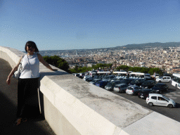 Miaomiao at the road to the Notre-Dame de la Garde basilica, with a view on the square in front with a tourist train and wooden cross, and the city center