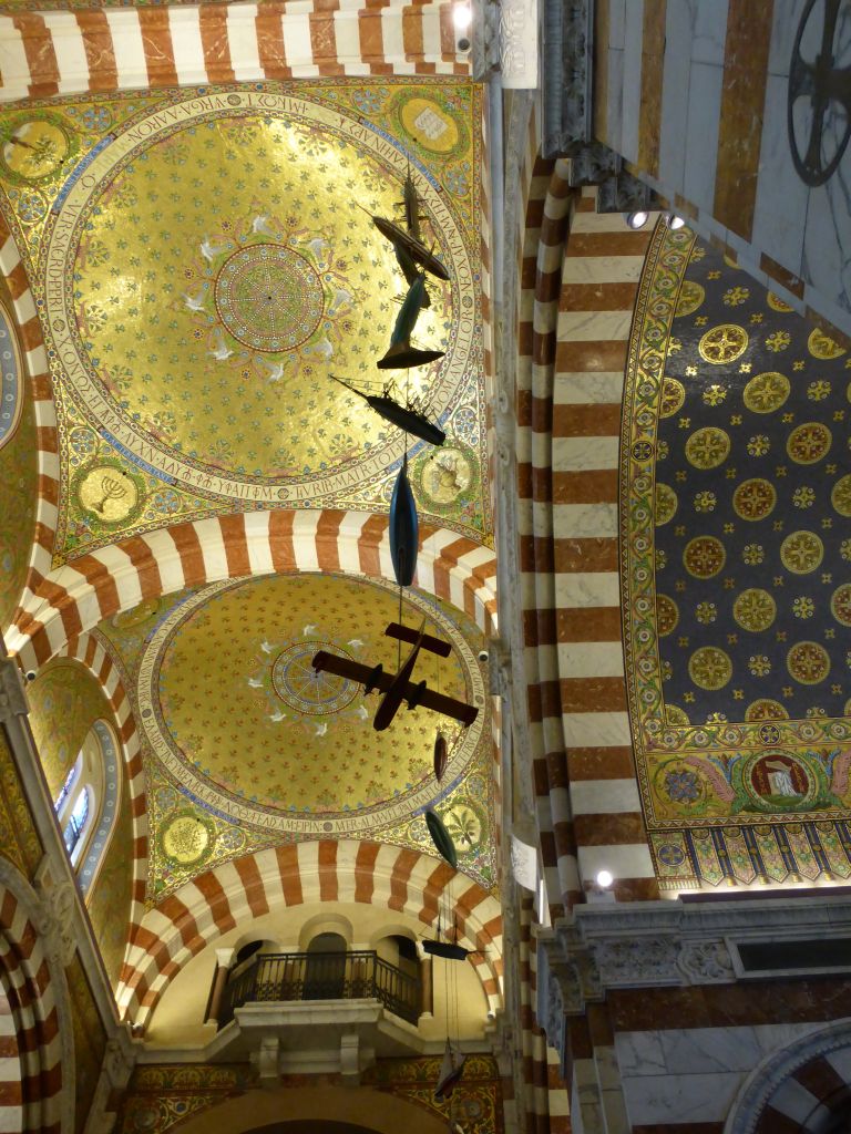 Small airplanes and boats hanging on the left side of the ceiling of the nace of the Notre-Dame de la Garde basilica