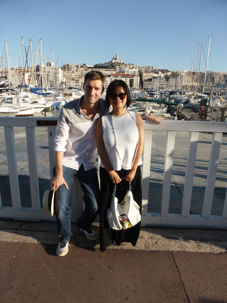 Tim and Miaomiao at the Quai du Port street with a view on the boats in the Old Port and the Notre-Dame de la Garde basilica