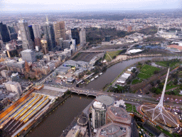 The Spire of the Arts Centre Melbourne, skyscrapers at the city center, the Flinders Street Railway Station, St. Paul`s Cathedral, Federation Square with the Australian Centre for the Moving Image, the Princess Bridge over the Yarra River, the Melbourne Cricket Ground and the Fitzroy Gardens, viewed from the Skydeck 88 of the Eureka Tower, at sunset