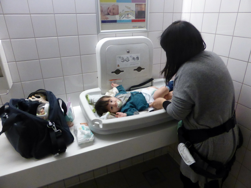 Miaomiao changing Max`s diaper in a changing room at the Departures Hall of Schiphol Airport