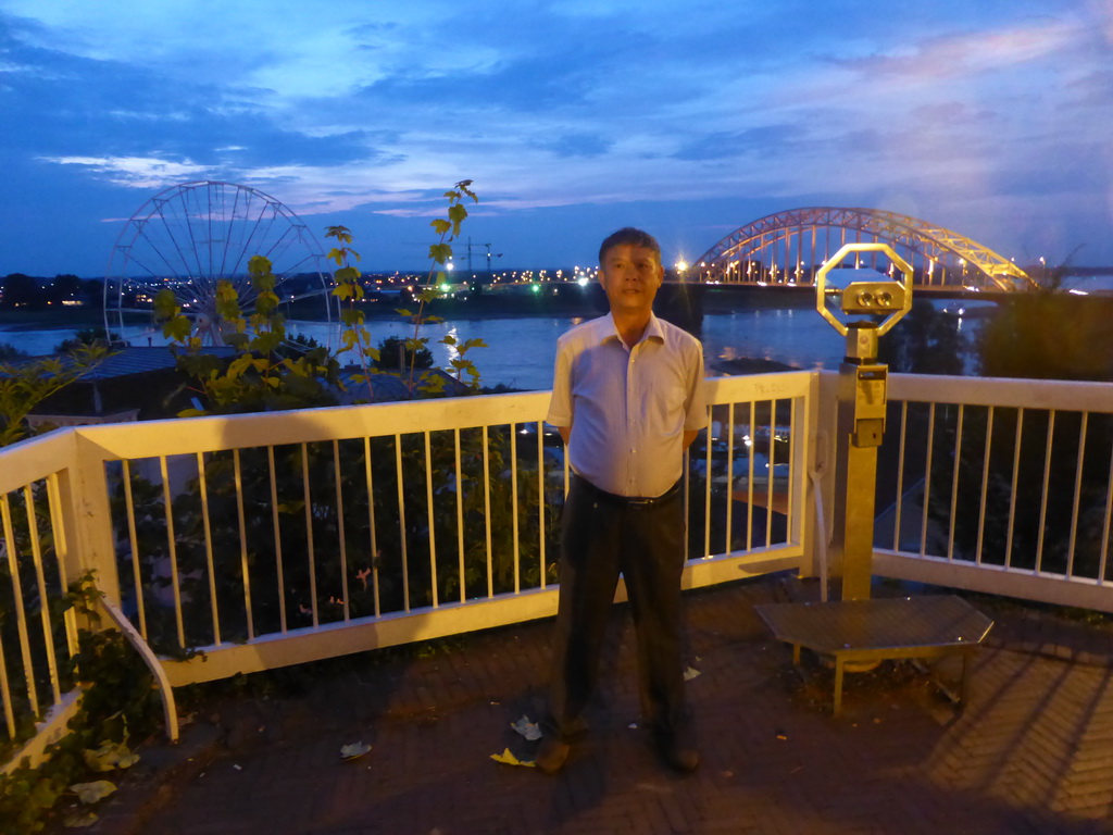 Miaomiao`s father at the northwest side of the Valkhof park, with a view on the Waalbrug bridge over the Waal river and a ferris wheel, at sunset