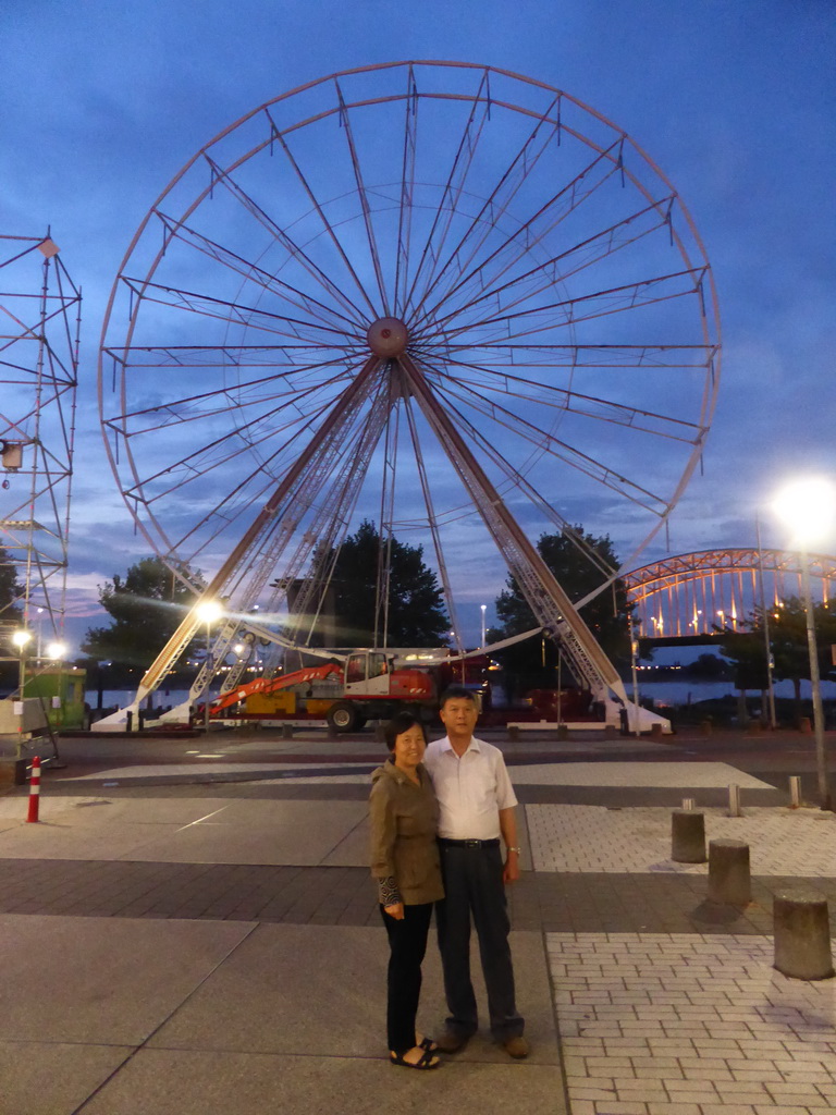 Miaomiao`s parents with the ferris wheel at the Waalkade promenade and the Waalbrug bridge over the Waal river, at sunset