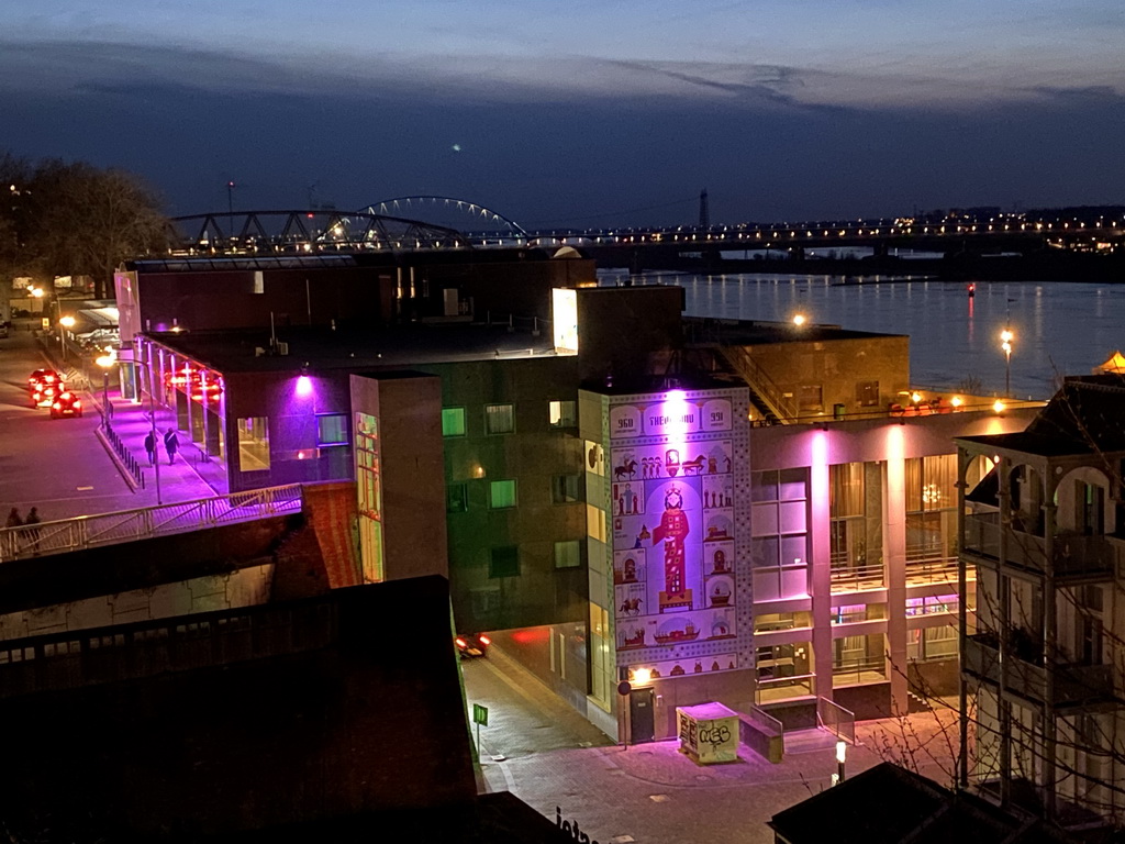 The Waal river with the Nijmegen railway bridge and the Oversteek bridge, the Groene Balkon and Vleeshouwerstraat streets and the `Prinses uit het Oosten` wall painting, viewed from the Valkhof park, by night