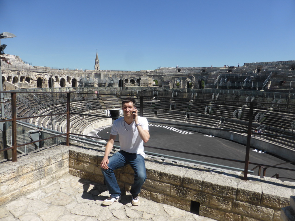 Tim at the upper middle rows of seats, with a view on the east side of the interior of the Arena of Nîmes and the tower of the Eglise Sainte Perpétue church