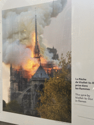 Photograph `The spire by Viollet-le-Duc in flames` at the exhibition `Notre-Dame de Paris - The first months of a renaissance` at the Rue du Cloître-Notre-Dame street, with explanation