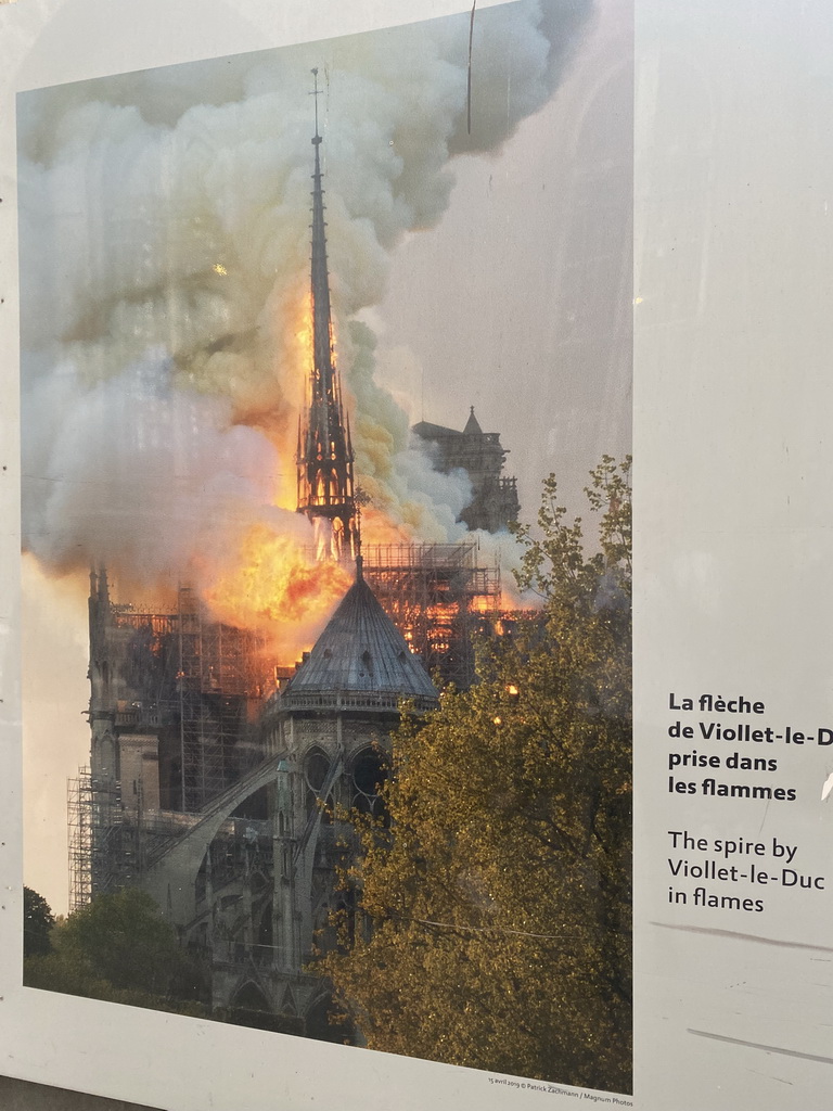 Photograph `The spire by Viollet-le-Duc in flames` at the exhibition `Notre-Dame de Paris - The first months of a renaissance` at the Rue du Cloître-Notre-Dame street, with explanation