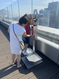 Miaomiao and Max looking through a telescope at the observation deck at the top floor of the Grande Arche de la Défense building, with a view on the skyscrapers at the La Défense district