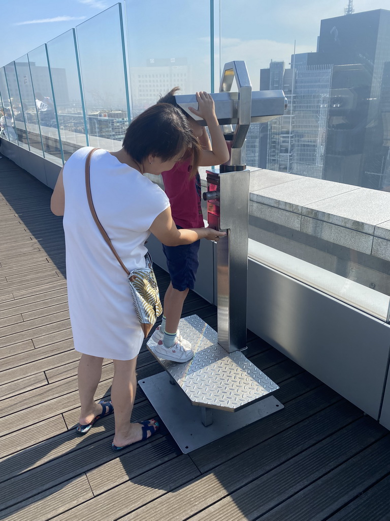 Miaomiao and Max looking through a telescope at the observation deck at the top floor of the Grande Arche de la Défense building, with a view on the skyscrapers at the La Défense district