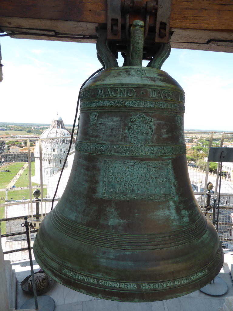 Bell at top floor of the Leaning Tower of Pisa, with a view on the Piazza del Duomo square with the Pisa Duomo cathedral and the Baptistry of St. John