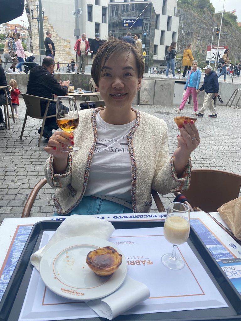 Miaomiao with a Pastéis de Nata and a drink at the terrace of the Flor de São Bento bakery at the Praça de Almeida Garrett square