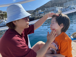 Miaomiao and Max putting on sunscreen on the deck of the Sagitarius Cat boat in the harbour