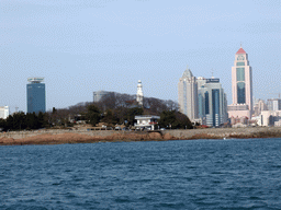 Xiao Qingdao island with its lighthouse in Qingdao Bay and skyscrapers at the city center, viewed from the tour boat