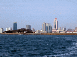 Xiao Qingdao island with its lighthouse and pavilion in Qingdao Bay and skyscrapers at the city center, viewed from the tour boat