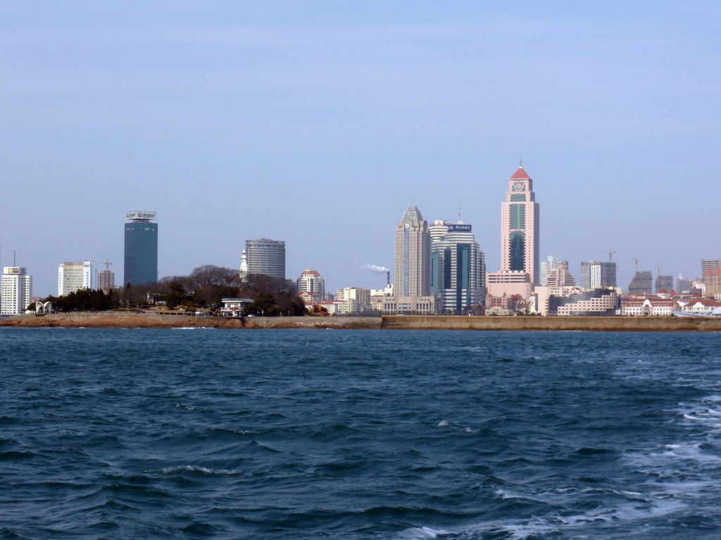 Xiao Qingdao island with its lighthouse and pavilion in Qingdao Bay and skyscrapers at the city center, viewed from the tour boat