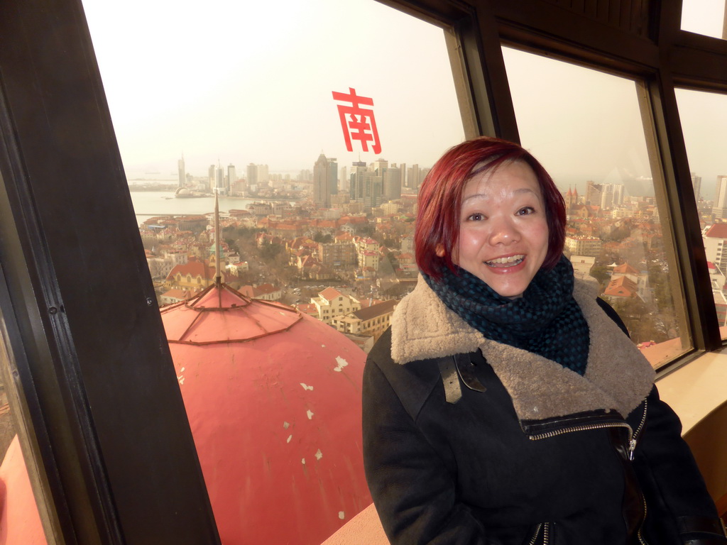 Miaomiao at the rotating sightseeing tower at the Xinhaoshan Park, with a view on the city center with skyscrapers, St. Michael`s Cathedral and the Qingdao Protestant Church, Qingdao Bay and the skyscrapers and dome at the west side of the city