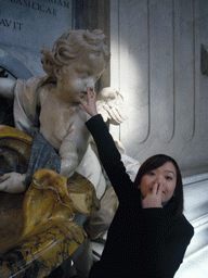 Miaomiao and the statue of a Cupido offering holy water, at the foot of the Monument of Pope Benedict XIII, inside St. Peter`s Basilica