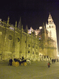 The east side of the Seville Cathedral with the Giralda tower and horse and carriage at the Plaza del Triunfo square, by night