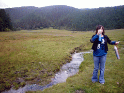 Miaomiao with oxygen bottle in grassland with yaks and stream in Potatso National Park
