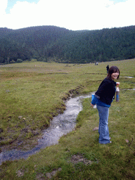Miaomiao with oxygen bottle in grassland with yaks and stream in Potatso National Park