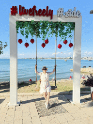 Miaomiao on a swing at the square at Nar Beach 1, with a view on boats in the Gulf of Antalya and beaches and hotels at the northwest side of town