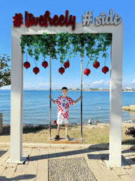Max on a swing at the square at Nar Beach 1, with a view on boats in the Gulf of Antalya and beaches and hotels at the northwest side of town