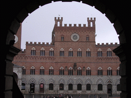 Front of the the Pubblico Palace at the Piazza del Campo square, viewed through an arch at the Loggia della Mercanzia building