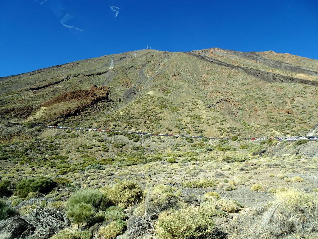 Mount Teide and cars parked in line on the road to the Teide Cable Car base station, viewed from the rental car on the TF-21 road