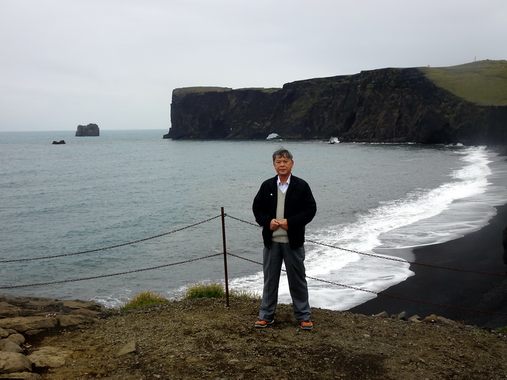 Miaomiao`s father at the lower viewpoint of the Dyrhólaey peninsula, with a view on the Rock Arch