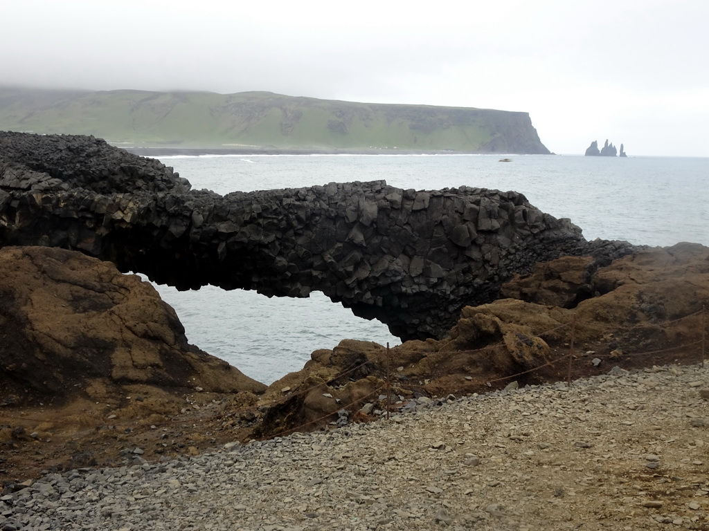 Small rock arch at the lower viewpoint of the Dyrhólaey peninsula, with a view on the Reynisfjara Beach and the Reynisdrangar rocks