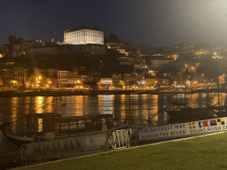 The ferry over the Douro river at the ferry dock at the Avenida de Diogo Leite street and Porto with the Cais da Ribeira street and the Paço Episcopal do Porto palace, by night
