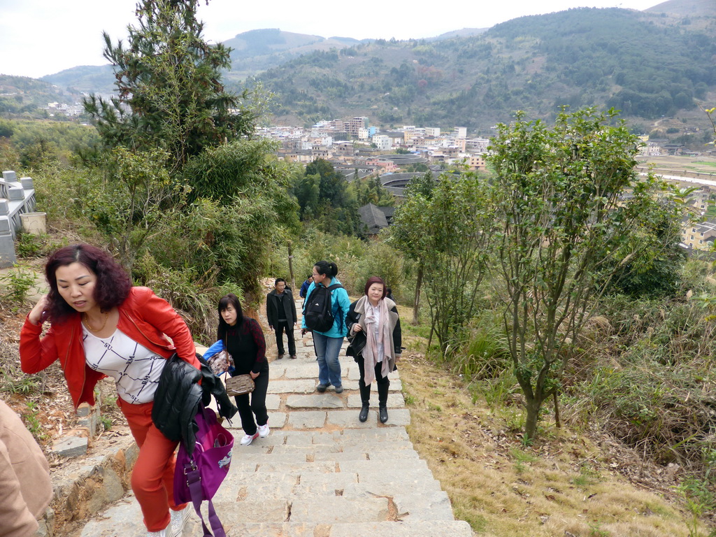 Miaomiao on the staircase to the Yongding Scenic Area viewing point, with a view on the Chengqi Lou and Beichen Lou buildings of the Gaobei Tulou Cluster