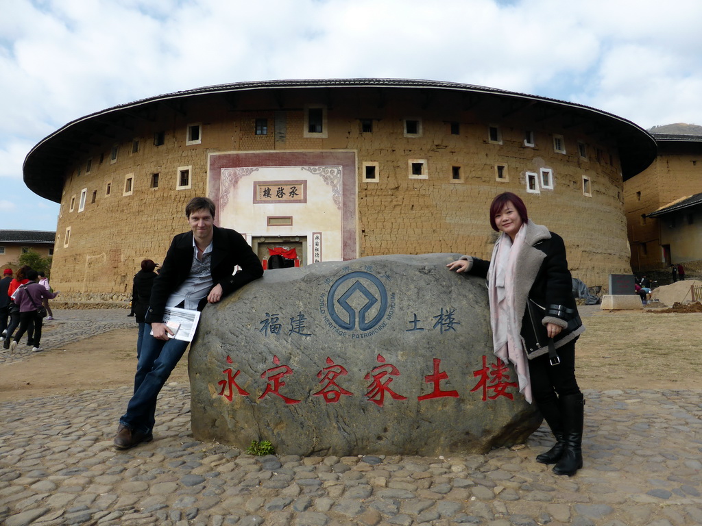 Tim and Miaomiao and a rock with the UNESCO World Heritage inscription in front of the Chengqi Lou building of the Gaobei Tulou Cluster