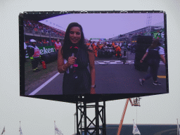 TV screen with interviewer and Formula 1 cars at the main straight at Circuit Zandvoort, viewed from the Eastside Grandstand 3, just before the Formula 1 Race